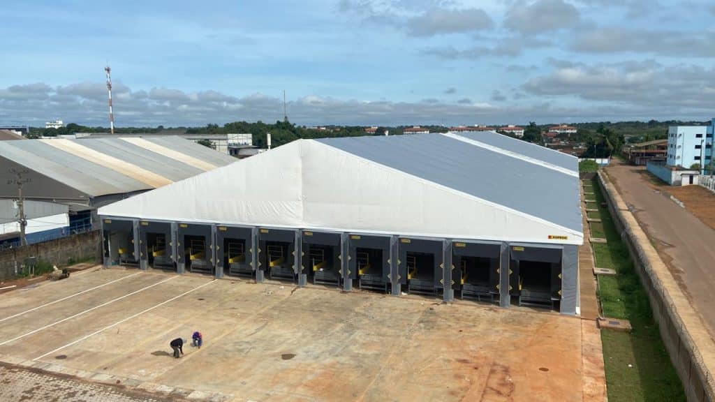 Galpão logístico com docas de carga, coberto por lona branca, em área industrial.